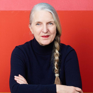 A picture of Anne Lise Kjaer, a futurist, in a navy blue turtle neck shirt against a red background.