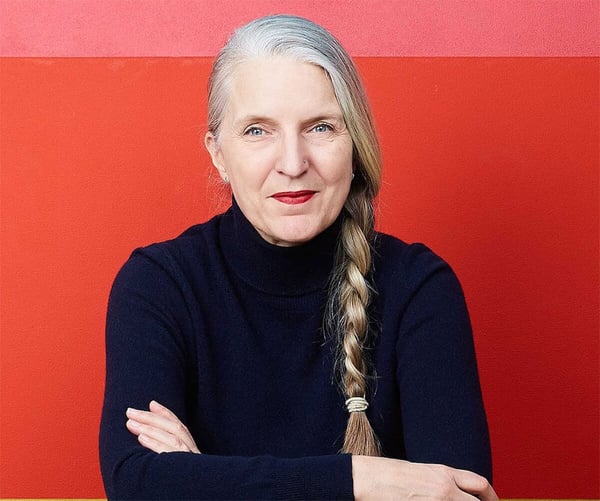 A picture of Anne Lise Kjaer, a futurist, in a navy blue turtle neck shirt against a red background.